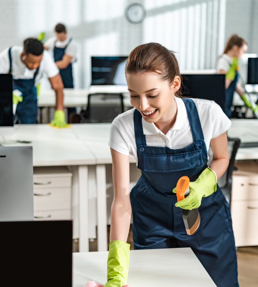 cheerful-cleaner-in-overalls-cleaning-office-desk-with-rag.jpg